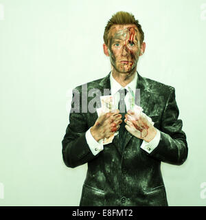 Blutiger Mann in einem schmutzigen Anzug, der eine Handvoll Geld hält Stockfoto