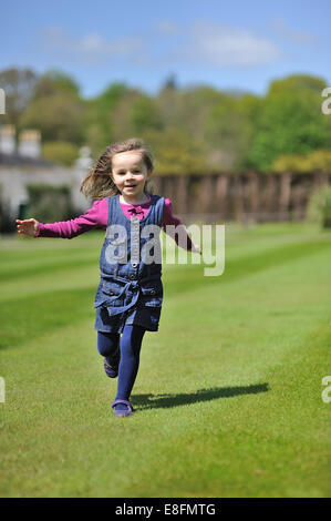 Kleines Mädchen (4-5) läuft auf dem grünen Rasen Stockfoto