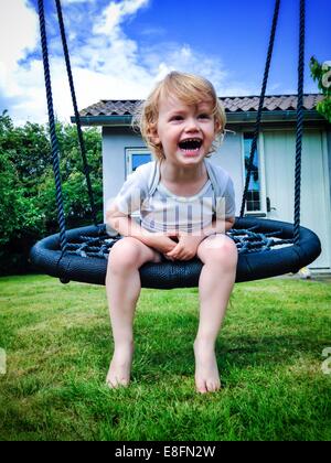 Junge sitzt auf der Schaukel im Garten Stockfoto