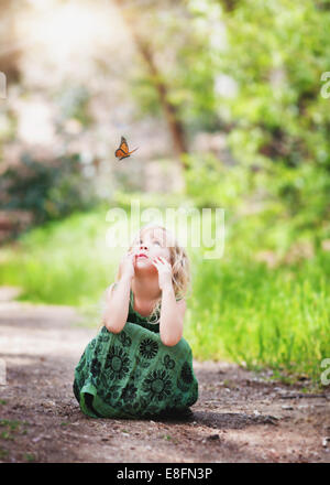 Mädchen auf einem Pfad sitzend, einen Schmetterling betrablickend, Kalifornien, USA Stockfoto