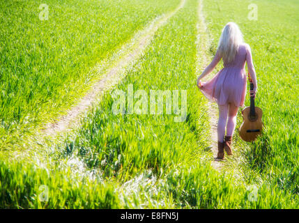 Rückansicht der jungen Frau zu Fuß auf der grünen Wiese mit Gitarre Stockfoto