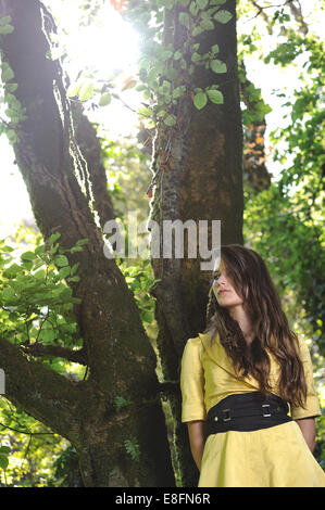 Junge Frau lehnte sich gegen Baum im Wald Stockfoto