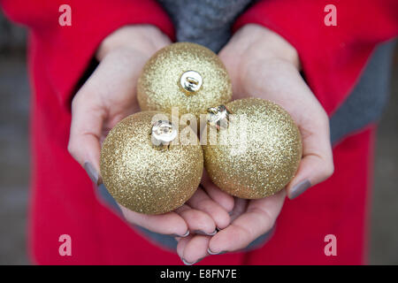 Nahaufnahme von Frauenhänden, die drei goldene Weihnachtskugeln halten Stockfoto