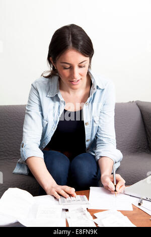 Junge Frau, die auf dem Sofa sitzt und für die Haushaltsfinanzen arbeitet Stockfoto