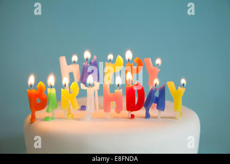Zündete Happy Birthday Kerzen auf einem Geburtstagskuchen an Stockfoto