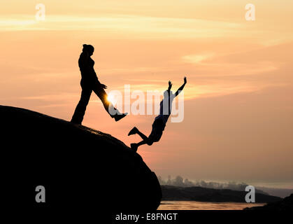 Silhouette eines Mannes auf Felsen treten eine Frau Stockfoto