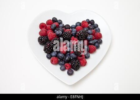 Blick von oben auf frische Brombeeren, Heidelbeeren und Himbeeren auf einem herzförmigen Teller Stockfoto