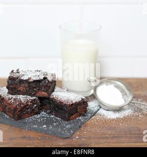 Schokoladen-Brownies bestäubt mit Puderzucker und Glas Milch Stockfoto