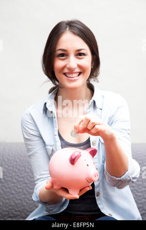 Porträt einer lächelnden jungen Frau, die eine Münze in ein Sparschwein steckt Stockfoto