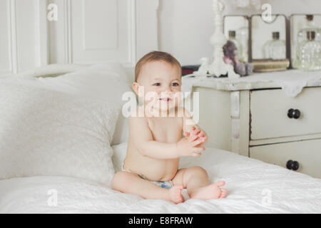 Porträt von Smiling Baby sitzt auf dem Bett im Schlafzimmer Stockfoto