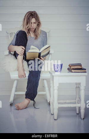 Porträt einer Frau, die auf einem Buch mit Tasse Tee Stuhl sitzend Stockfoto
