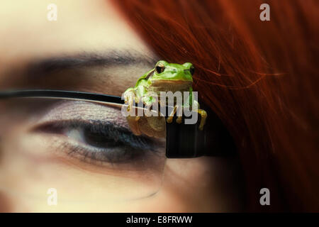 Nahaufnahme eines Miniaturfrosches, der auf der Brille einer Frau sitzt Stockfoto