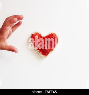 Junge Griff nach herzförmige Scheibe Brot und Marmelade Stockfoto