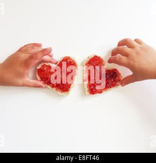 Zwei jungen Griff nach herzförmige Scheibe Brot und Marmelade Stockfoto