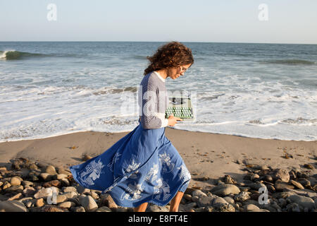 Frau, die am Strand entlang läuft und eine Schreibmaschine trägt Stockfoto