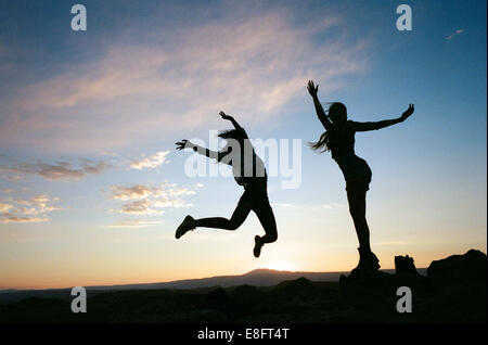 Silhouetten von zwei Frauen, die bei Sonnenuntergang in der Luft springen Stockfoto