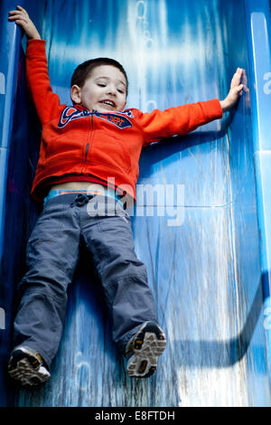 Junge rutscht Folie auf Spielplatz Stockfoto