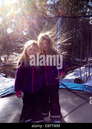 Zwei Mädchen mit statischem Haar stehen auf einem Trampolin im Garten, Schweden Stockfoto