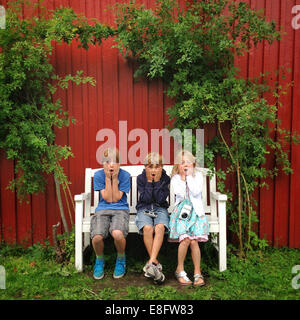 Drei Kinder sitzen auf Bank im Garten Stockfoto