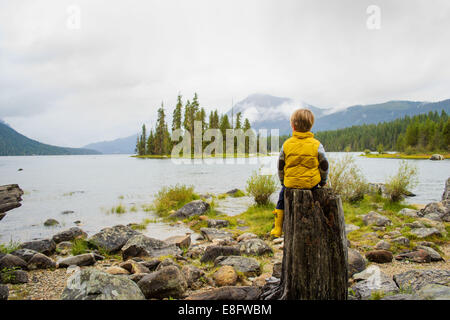 Junge sitzt auf einem Baumstamm an einem See, USA Stockfoto