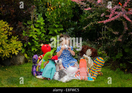Mädchen sitzt im Garten mit Tee-Party mit ihrem Spielzeug Stockfoto