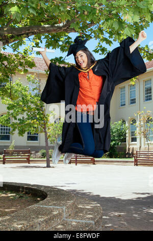 Junge weibliche Absolventin in die Luft springen Stockfoto