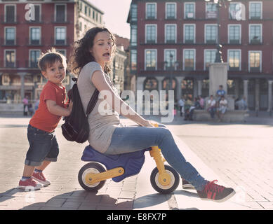 Junge Drängen seiner Mutter auf einem Spielzeug Dreirad Stockfoto