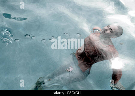 Voll bekleidete Frau mit geschlossenen Augen schwimmend unter Wasser in einem Schwimmbad Stockfoto
