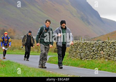 Wanderer aus einen Land Rover und Royal Navy Auswahlmannschaft zu Fuß entlang einer Landstraße nach dem Abstieg Skafell Hecht Stockfoto