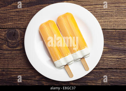 Zwei orange Eis am Stiel in Platte auf Holztisch. Ansicht von oben Stockfoto