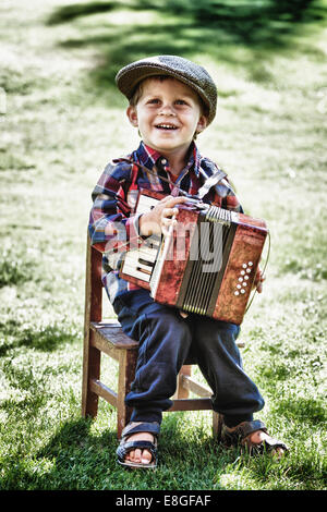 glücklicher Junge trägt retro oder Vintage Stil spielt Akkordeon im Freien im Garten im Sommer Stockfoto