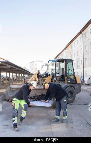 Arbeitnehmer, die Analyse der Blaupause vor Bagger auf Baustelle Stockfoto