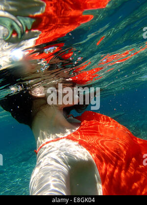 Nahaufnahme einer Frau in einem Kleid, die unter Wasser schwimmt, Sounion, Lavreotiki, Griechenland Stockfoto