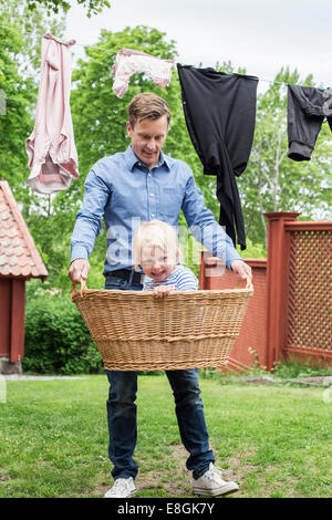 Volle Länge des spielerischen Vater mit Tochter im Korb am Hof Stockfoto