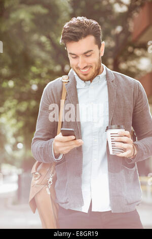 Lächelnd Geschäftsmann Kaffeetrinken beim Lesen von SMS-Nachricht auf Smartphone im freien Stockfoto