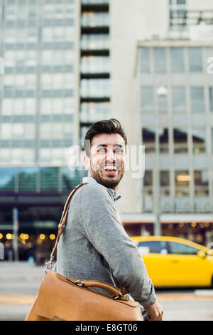 Glücklich Kaufmann wegschauen während des Tragens Umhängetasche auf Stadtstraße Stockfoto