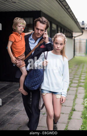 Geschäftsmann mit Handy bei einem Spaziergang mit den Kindern im Hof Stockfoto