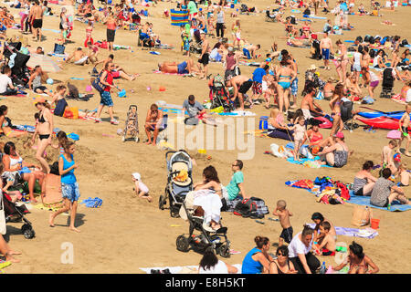 Menschen genießen den Sonnenschein an einem überfüllten Strand in Folkestone. Stockfoto