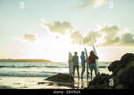 Drei Jugendliche stehen am Strand mit ihren Surfbrettern Blick auf Horizont Stockfoto