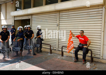 Athen, Griechenland. 8. Oktober 2014. Ein Demonstranten sitzt draußen das Innenministerium, neben der Riot-Polizisten, die den Eingang bewachen. Die griechische Gemeinde Workers' Union (POE-OTA) protestierten außerhalb der Ministerium der Verwaltungsreform gegen Lohnkürzungen, Entlassungen in der lokalen Regierung und lokale Regierungsreformen. Die Demonstranten zogen später zu den. Ministerium des Innern. Bildnachweis: Michael Debets/Alamy Live-Nachrichten Stockfoto