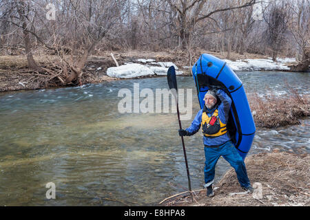 Senioren männlich tragen eine Packraft (ein-Personen-leichte Floß zur Expedition oder Multisport) am Fluss-Ufer Stockfoto