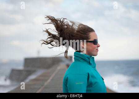 Ein junge weibliche Mädchen steht mit Blick in den Wind mit ihren Haaren weht hinter ihr. Stockfoto