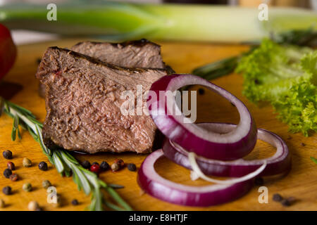 In Scheiben geschnittene Rindfleisch und roten Zwiebeln auf Schneidebrett mit anderen Zutaten Stockfoto