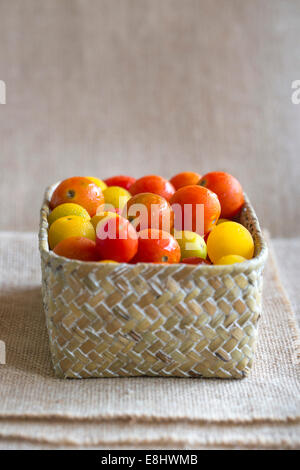 saftige rote und gelbe Kirschtomaten in geflochtenen Korb Creme Tuch Hintergrund Stockfoto