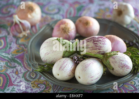 vergoldete weißen Auberginen mit lila feine Streifen, Zwiebel und Knoblauch gegen lila floral Tischdecke Stockfoto