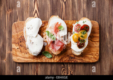 Drei Bruschetta mit Mozzarella-Käse, Schinken und gebratenen Tomaten auf Ciabatta-Brot auf hölzernen Hintergrund Stockfoto