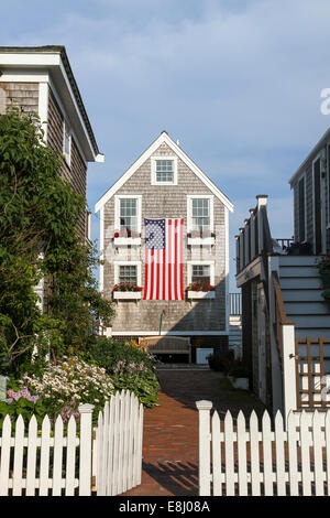 Ein Tor öffnet sich nach einem hübschen Häuschen mit Blumenkästen auf Windows, drapiert mit einem großen amerikanischen Flagge. Provincetown, Cape Cod Stockfoto