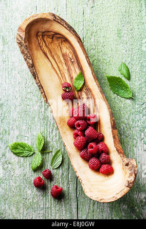 Himbeeren mit Blättern aus Olivenholz Schale auf grünem Hintergrund aus Holz Stockfoto