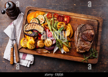 Club-Rindersteak und gegrilltes Gemüse auf Schneidebrett auf dunklem Holz Stockfoto