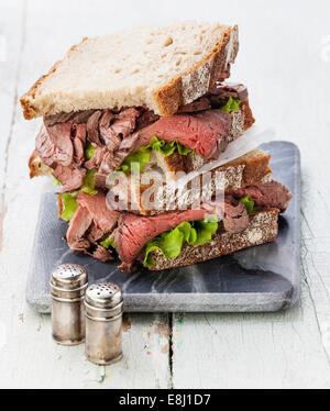 Roast Beef Sandwiches mit Salat auf Marmor Schneidebrett auf blauem Hintergrund Stockfoto